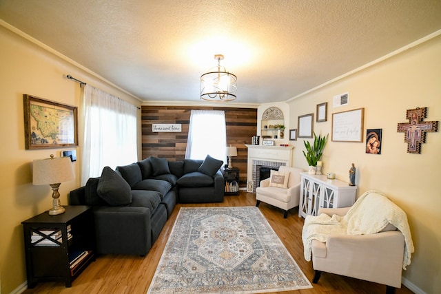 living area with a textured ceiling, wood finished floors, a brick fireplace, a chandelier, and built in features