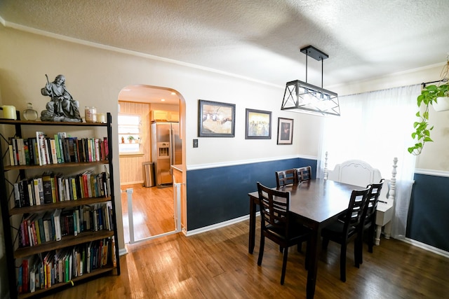dining space with arched walkways, a textured ceiling, wood finished floors, and baseboards