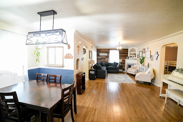 dining space featuring a textured ceiling, arched walkways, light wood finished floors, crown molding, and a fireplace