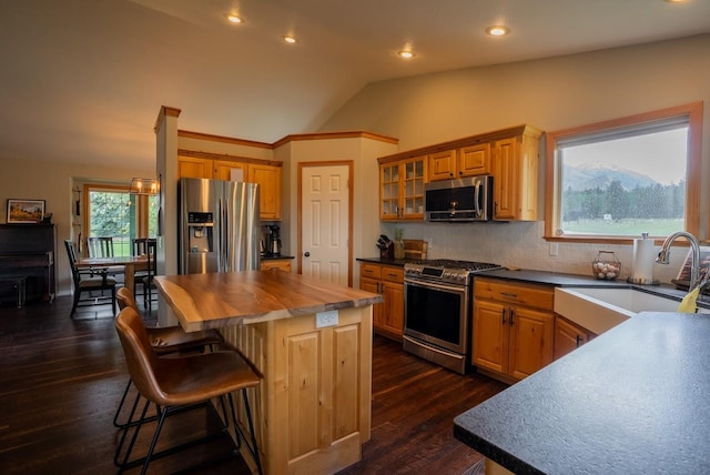 kitchen featuring appliances with stainless steel finishes, a sink, lofted ceiling, a kitchen island, and a kitchen bar