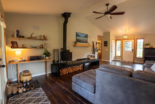 living room featuring a wood stove, wood finished floors, a ceiling fan, lofted ceiling, and baseboards