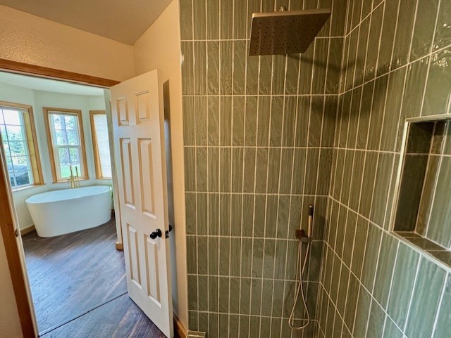 bathroom featuring a walk in shower, a freestanding bath, and wood finished floors