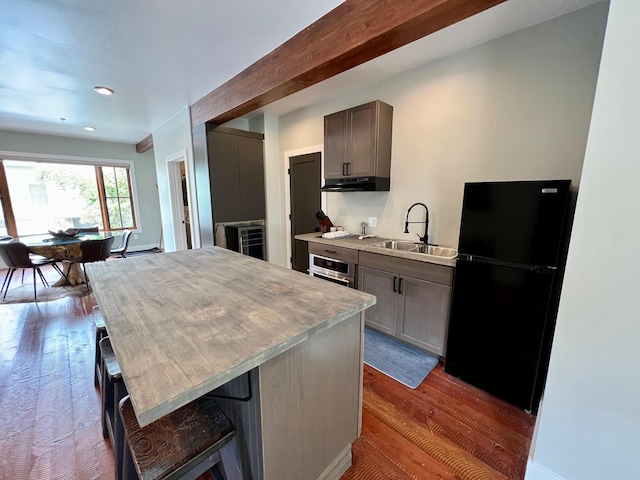 kitchen with freestanding refrigerator, a sink, stainless steel oven, under cabinet range hood, and dark wood-style floors