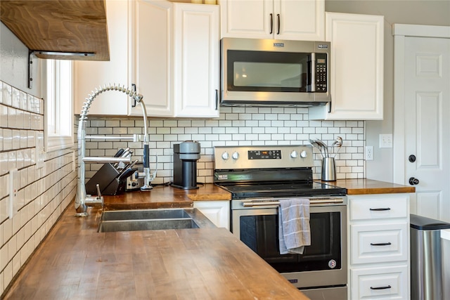 kitchen with stainless steel appliances, butcher block countertops, white cabinets, a sink, and backsplash