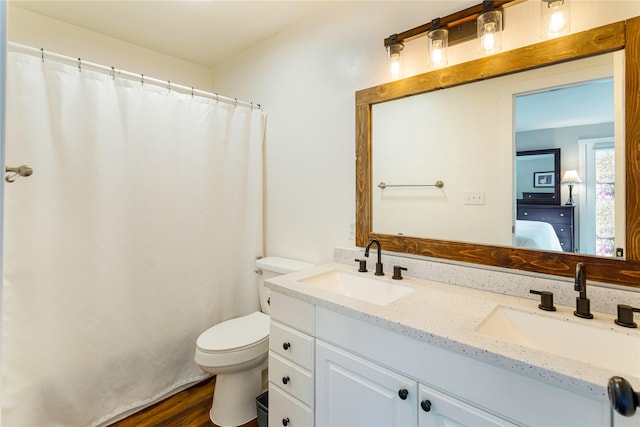 ensuite bathroom featuring toilet, double vanity, and wood finished floors