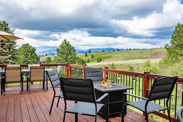 wooden terrace featuring a fire pit, outdoor dining area, a mountain view, and a view of rural / pastoral area