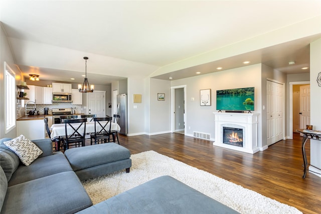 living room with dark wood finished floors, recessed lighting, a chandelier, a glass covered fireplace, and baseboards
