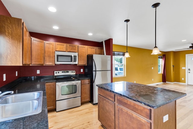 kitchen featuring appliances with stainless steel finishes, a sink, light wood-style floors, pendant lighting, and a kitchen island