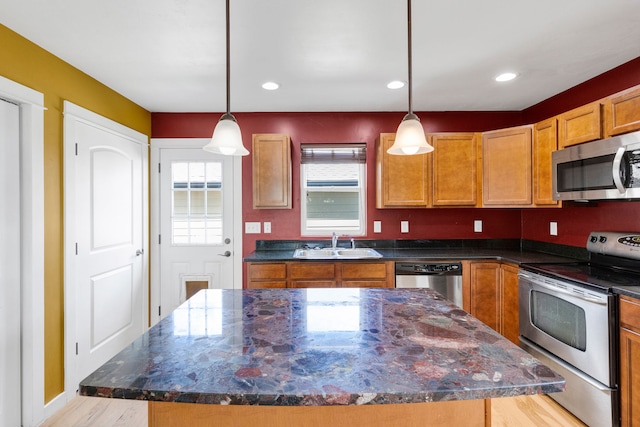 kitchen with appliances with stainless steel finishes, a sink, light wood-style flooring, a kitchen island, and pendant lighting