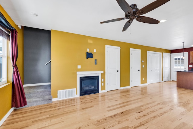 unfurnished living room featuring baseboards, a glass covered fireplace, light wood-type flooring, and a ceiling fan