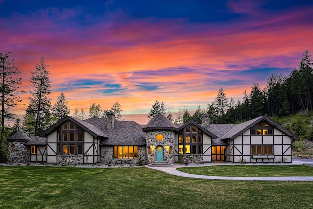 215 Browns Gulch Rd, Kalispell, MT 59901 - back of property at dusk featuring stone siding, a yard, a chimney, and stucco siding