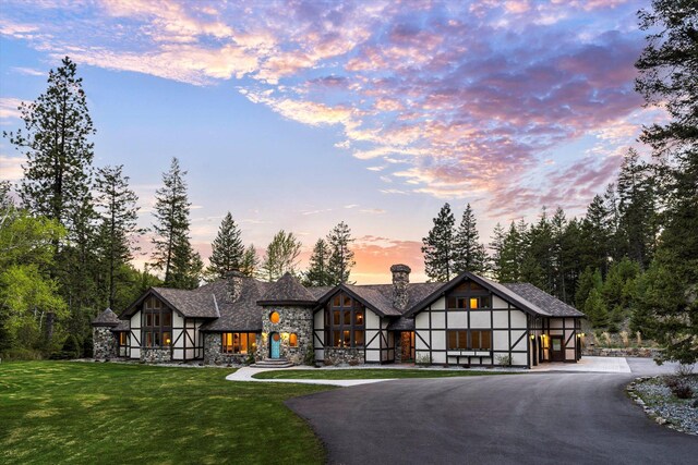 215 Browns Gulch Rd, Kalispell, MT 59901 - tudor-style house with stone siding, curved driveway, a front lawn, a chimney, and stucco siding