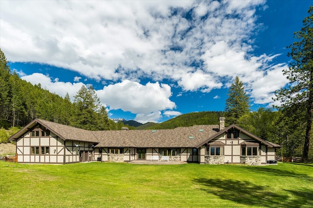 215 Browns Gulch Rd, Kalispell, MT 59901 - rear view of house featuring stone siding, a chimney, a yard, a patio, and a mountain view