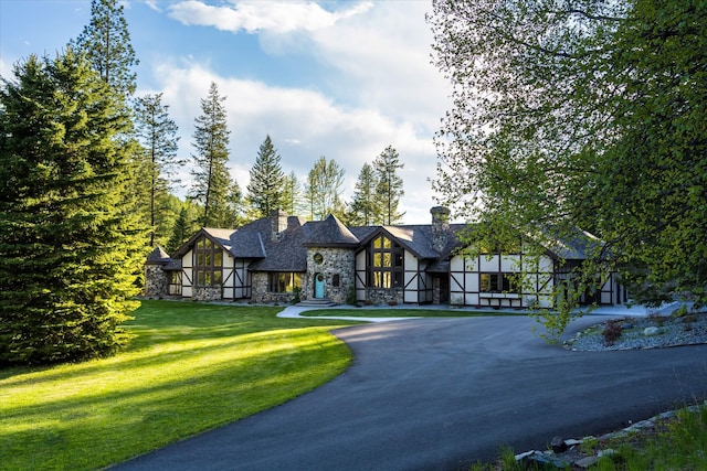 215 Browns Gulch Rd, Kalispell, MT 59901 - tudor-style house with stone siding, curved driveway, a front lawn, and a chimney