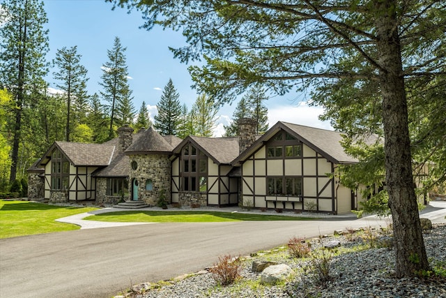 215 Browns Gulch Rd, Kalispell, MT 59901 - tudor house with stucco siding, stone siding, a chimney, driveway, and a shingled roof
