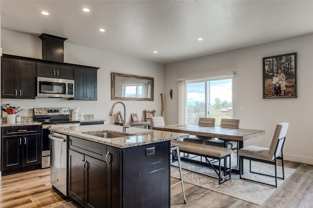 kitchen featuring stainless steel appliances, a sink, light wood-style flooring, recessed lighting, and a center island with sink