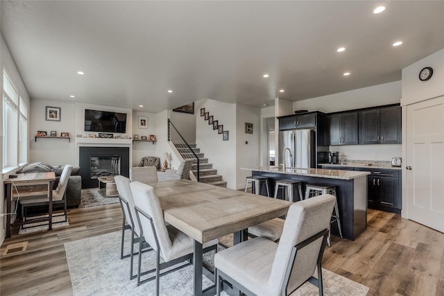 dining area with a glass covered fireplace, stairway, recessed lighting, and light wood-type flooring