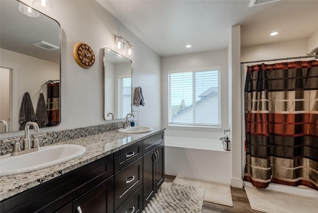 bathroom with wood finished floors, a bath, double vanity, curtained shower, and recessed lighting