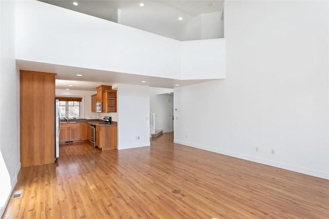 2060 Marina Ct, Bigfork, MT 59911 - unfurnished living room with light wood-style flooring, recessed lighting, baseboards, a high ceiling, and a sink