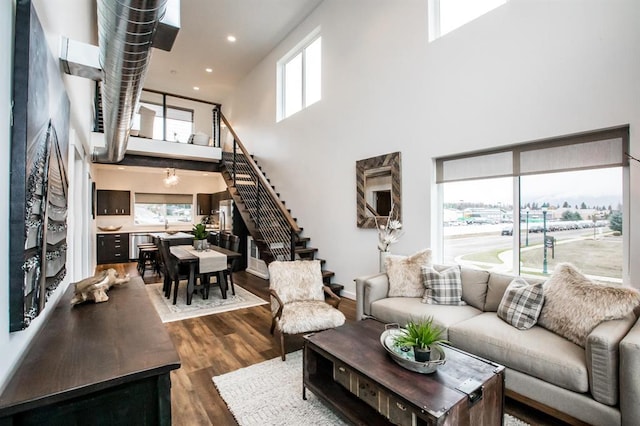 living room featuring stairway, a towering ceiling, dark wood finished floors, healthy amount of natural light, and recessed lighting