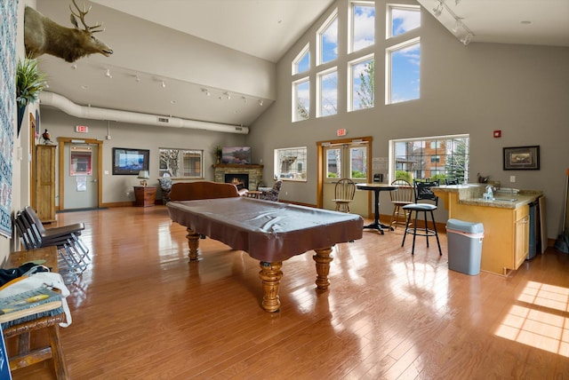 playroom featuring billiards, a lit fireplace, light wood finished floors, healthy amount of natural light, and high vaulted ceiling