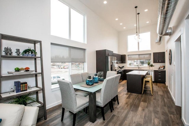 dining area featuring a high ceiling, dark wood-type flooring, plenty of natural light, recessed lighting, and baseboards