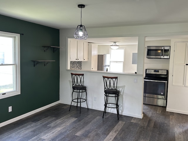 kitchen featuring stainless steel appliances, dark wood-style flooring, a breakfast bar, white cabinets, and baseboards