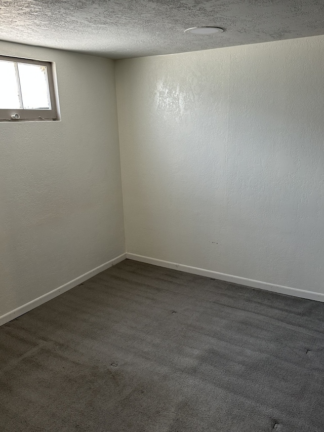 empty room with a textured ceiling, dark colored carpet, and baseboards