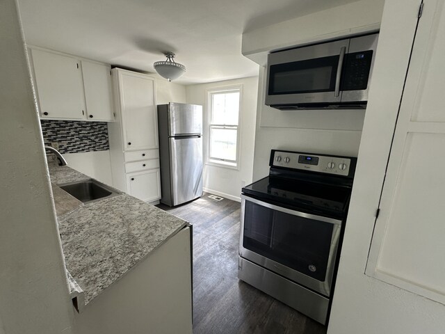 kitchen featuring appliances with stainless steel finishes, a sink, dark wood finished floors, white cabinetry, and backsplash