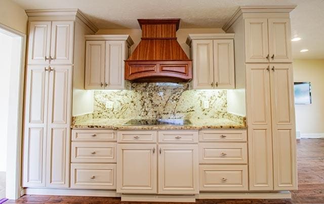 6 Cedar Lake Dr, Butte, MT 59701 - kitchen featuring custom exhaust hood, cream cabinetry, black electric cooktop, tasteful backsplash, and light stone counters