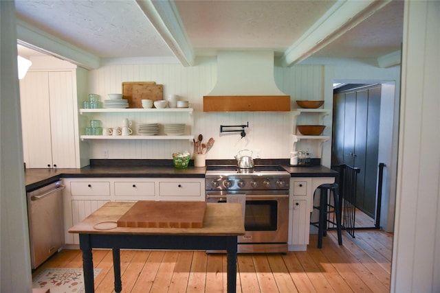 kitchen with stainless steel appliances, premium range hood, beamed ceiling, dark countertops, and light wood-style flooring