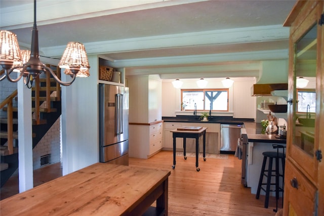 kitchen with stainless steel appliances, a chandelier, light wood-style flooring, dark countertops, and a sink