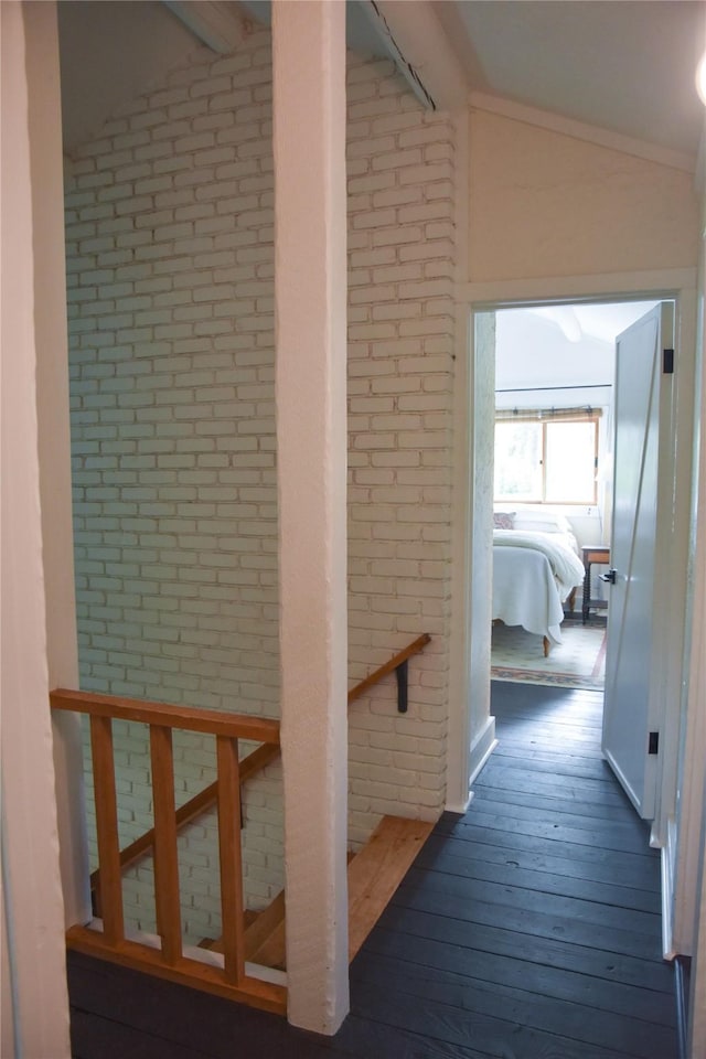 corridor with lofted ceiling, brick wall, and hardwood / wood-style flooring
