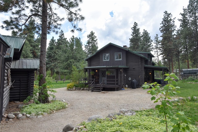 back of house featuring log siding, dirt driveway, covered porch, and metal roof