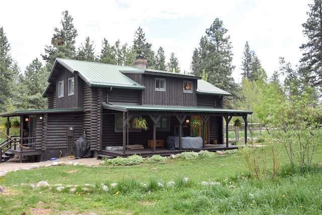 back of property featuring a chimney, metal roof, and a lawn
