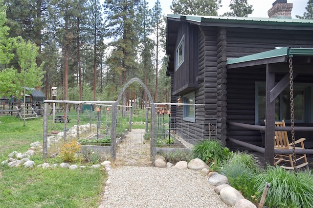 view of home's exterior with a garden, a chimney, log exterior, metal roof, and fence