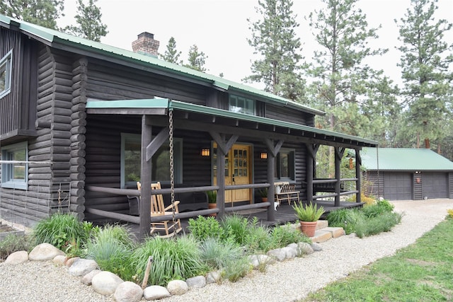 view of front of property featuring a porch, a chimney, log siding, metal roof, and a garage
