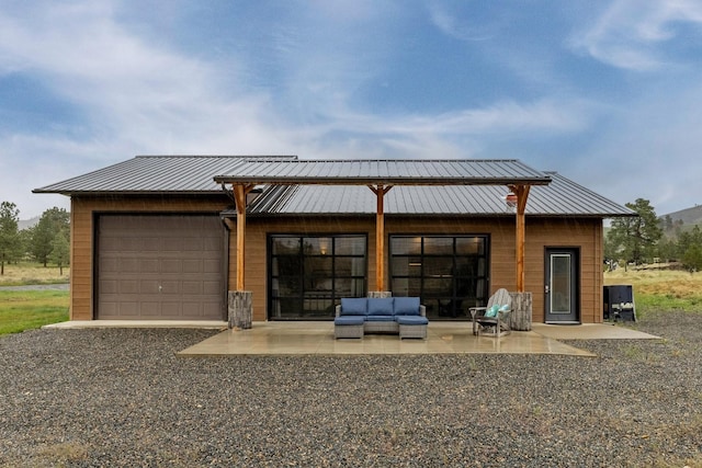 back of house with outdoor lounge area, a garage, a patio, driveway, and metal roof