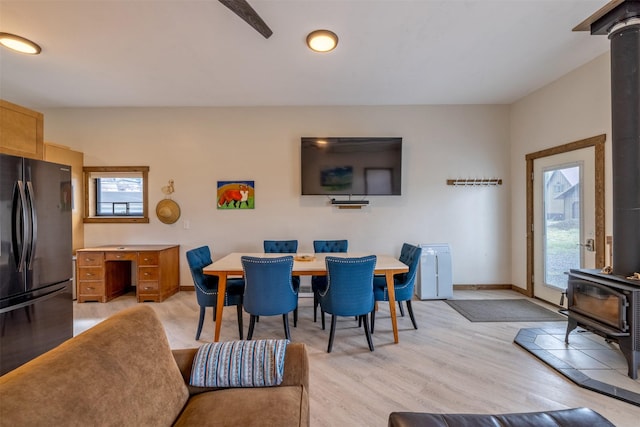 dining area featuring a wood stove, light wood-style flooring, and baseboards