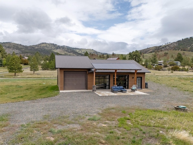 view of front of property featuring a mountain view, a garage, gravel driveway, an outdoor living space, and metal roof
