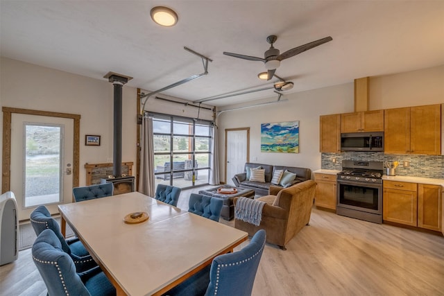 dining room with a wood stove, light wood finished floors, and ceiling fan