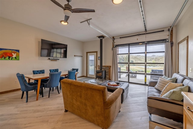 living room with a wood stove, light wood-style flooring, ceiling fan, and baseboards