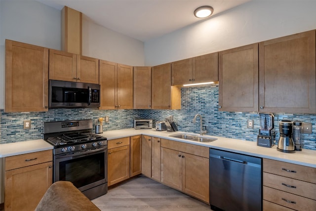 kitchen with appliances with stainless steel finishes, a sink, backsplash, and light countertops