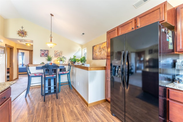 kitchen featuring black fridge with ice dispenser, vaulted ceiling, wood finished floors, hanging light fixtures, and light stone countertops
