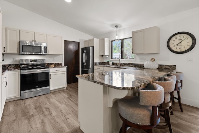 135 Sapphire Ct, Whitefish, MT 59937 - kitchen featuring appliances with stainless steel finishes, a breakfast bar, vaulted ceiling, dark stone countertops, and a peninsula