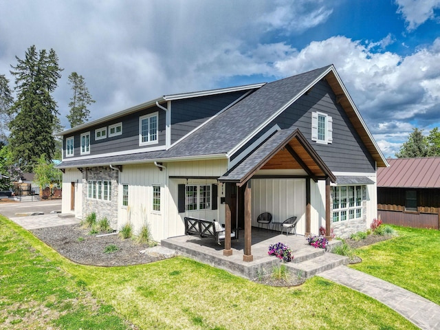 back of house featuring stone siding, a patio, a lawn, and a shingled roof