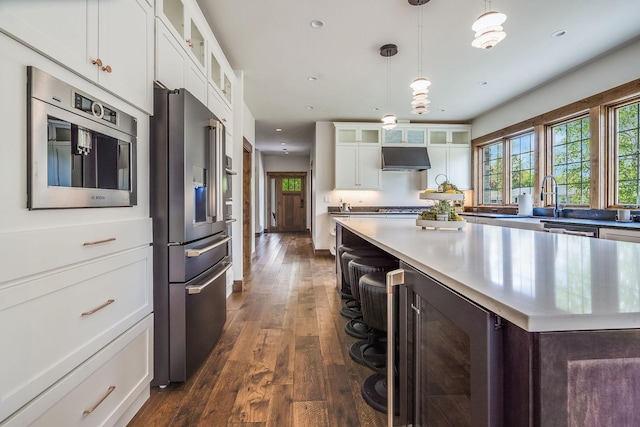 kitchen with appliances with stainless steel finishes, beverage cooler, dark wood finished floors, white cabinets, and light countertops