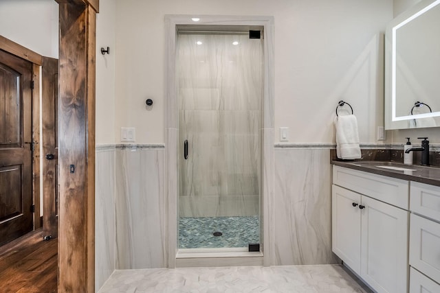 bathroom with a shower stall, a wainscoted wall, vanity, and tile walls