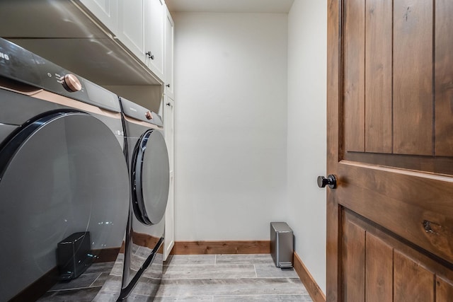 washroom with cabinet space, washer and clothes dryer, light wood-type flooring, and baseboards