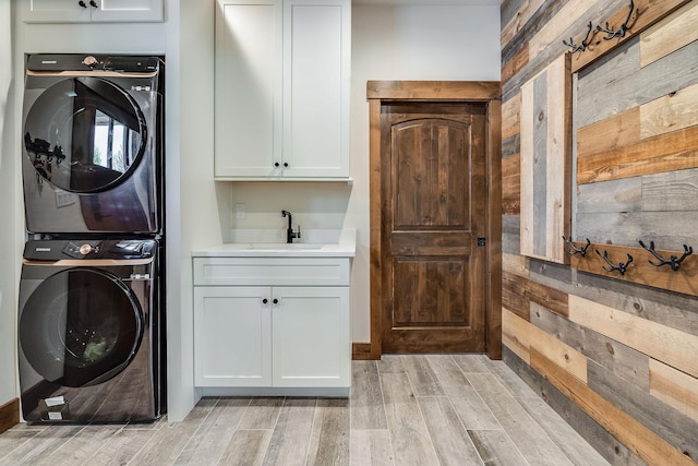 laundry room featuring cabinet space, stacked washer / dryer, light wood finished floors, wood walls, and wet bar